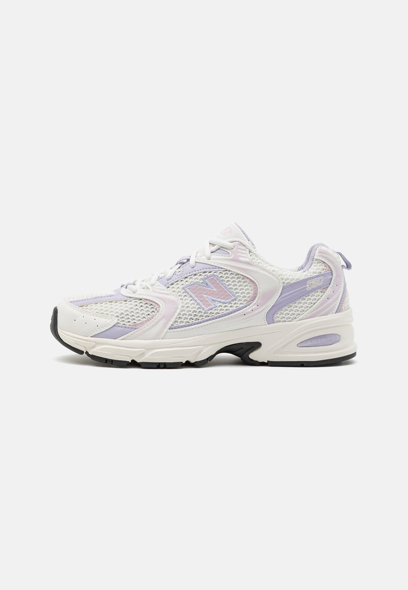 Scarpa sportiva bianca con tomaia in rete, accentata da dettagli viola, superficie texturizzata e colletto imbottito. Presenta una suola nera spessa per un maggiore supporto.