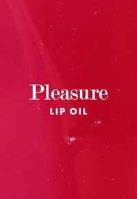 Olio labbra rosso con finitura lucida, arricchito da fini particelle di glitter. Il testo recita "Pleasure" sopra "LIP OIL" in caratteri bianchi e audaci.