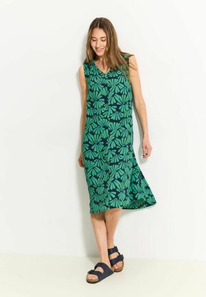 Vestito senza maniche verde con motivo floreale, scollatura a V e silhouette a trapezio, abbinato a sandali blu scuro. Tessuto dalla consistenza liscia.