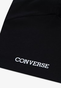 Svart bomullstyg med en slät struktur har den vita "CONVERSE"-logotypen broderad nära nederkanten. Enkel, ren design.