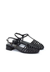 Sandalias de cuero negro con un diseño de tiras, tacón bajo y correa ajustable en el tobillo; presentan una textura suave y una estética minimalista.