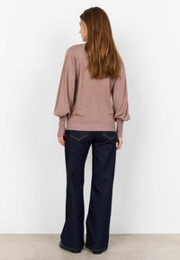 Pull en tricot marron avec des manches bouffantes, associé à un jean foncé évasé. Le tissu semble doux, avec une taille côtelée.