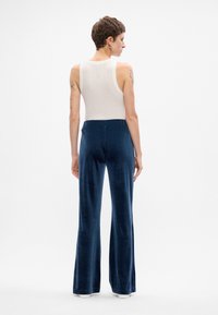 Tumši zila samta platās kājas bikses ar mīkstu tekstūru, ar gludu jostasvietu un vienu aizmugurējo kabatu, stilizētas ar pieguļošu balto bezpiedurkņu topu.