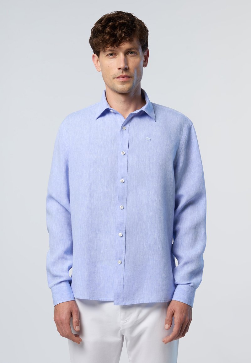 Maglietta azzurra chiara con maniche lunghe e bottoni bianchi, dotata di una texture sottile. Presenta un colletto classico e un piccolo emblema sul petto.