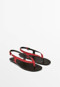 Rote Wildleder- und schwarze Leder-Sandalen mit flacher Sohle, offenen Zehen und verstellbarem Knöchelriemen. Nahtlose Textur und minimalistische Akzente.