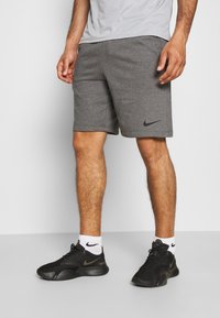 Grå idrottsshorts med en slät textur, med en svart Nike-logotyp på vänster ben. Bärs med svarta sneakers och vita strumpor.