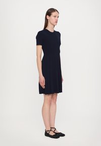 Navy ribbed dress with short sleeves and a pleated skirt. Paired with black polka dot flats featuring crisscross straps.