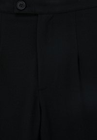 Zwarte broek van een gladde stof met een getailleerde pasvorm, met een enkele knoopsluiting en voorzijde plooien, die eenvoudige lijnen en stiksels toont.