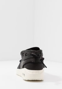 Musta nahkasneakeri, jossa on valkoinen pohja, näkyvä ilmatasku, ommeltuja yksityiskohtia ja sidottu nauha takana valkoisella pinnalla.