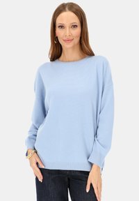 Jasnoniebieski sweter z dzianiny o okrągłym dekolcie, długich rękawach i luźnym kroju. Żebrowany dół i mankiety, miękka tekstura, zestawiony z ciemnymi dżinsami.