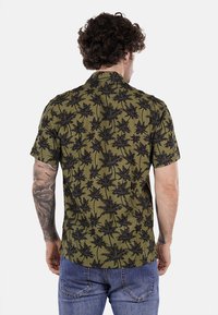 Camicia a maniche corte di colore verde oliva con un motivo di palme nere. Il tessuto appare leggero e con una vestibilità rilassata. Presenta un design del colletto classico.