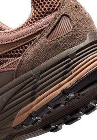 Επαναληπτική όψη της φτέρνας αθλητικού καφέ χρώματος που εμφανίζει υφή από σουέτ, επάνω μέρος από δίχτυ, πολυεπίπεδη σόλα και μαύρη λαστιχένια εξωτερική σόλα με λεπτομέρειες πέλματος.