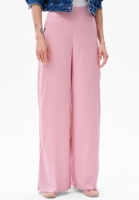 Jasnoróżowe spodnie o szerokich nogawkach, wykonane z miękkiego materiału, z wysokim stanem i gładką fakturą. Stylizowane z dżinsową kurtką i prostymi butami.