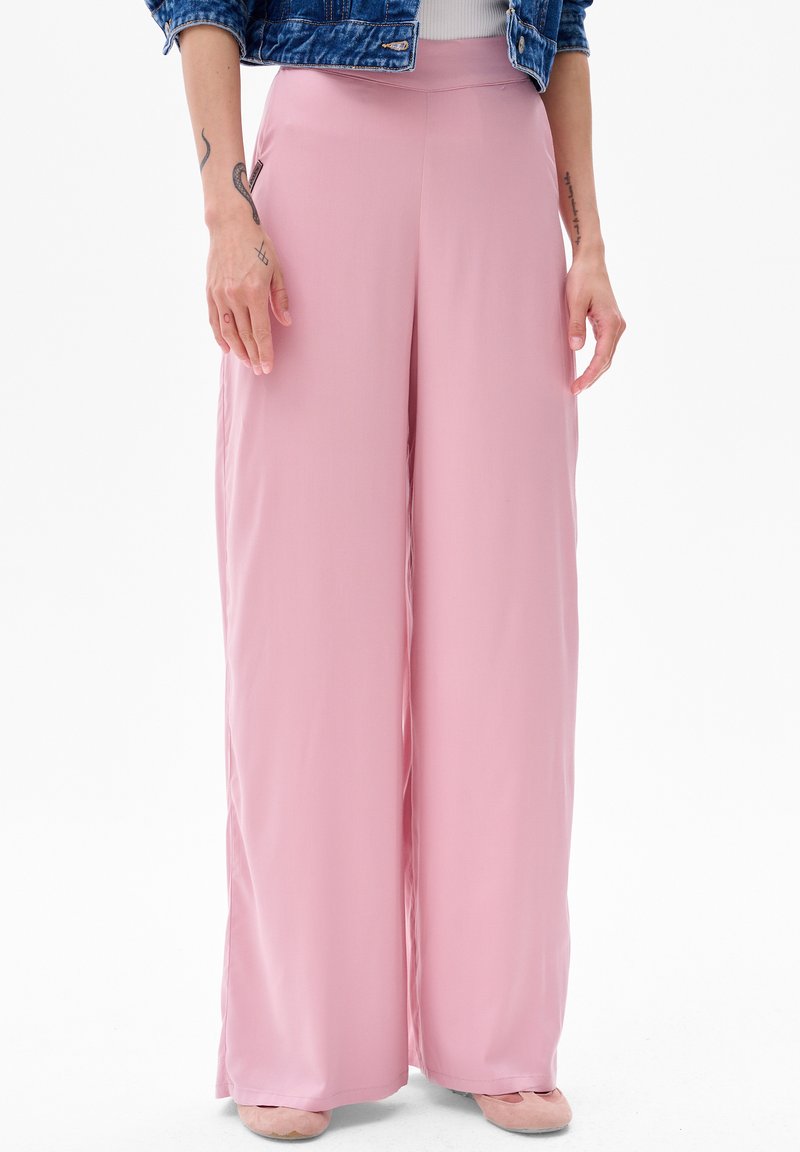 Jasnoróżowe spodnie o szerokich nogawkach, wykonane z miękkiego materiału, z wysokim stanem i gładką fakturą. Stylizowane z dżinsową kurtką i prostymi butami.