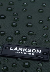 Zöld, textúrájú szövet vízcseppekkel. Fekete címke, amelyen fehér betűkkel olvasható: "LARKSON HAMBURG". A felület vízálló minőséget tükröz.