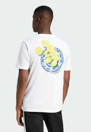 T-shirt bianco in cotone con una placca blu e limoni gialli e fette sul retro. Maniche corte e vestibilità rilassata.