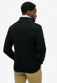 Czarny sweter z dzianiny z wysokim kołnierzem i prążkowanymi brzegami. Posiada długie rękawy i jednolitą teksturę. Nosi się go na jasnej koszuli.