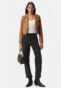 Cazadora biker de ante marrón sobre un camisola blanca, jeans negros de talle alto y botines negros. Bolso verde con cadena.