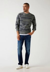 Sivý sveter s námorníckymi horizontálnymi pruhmi, okrúhlym výstrihom a rebrovaným lemom; v kombinácii s tmavomodrými džínsami a bielymi teniskami.