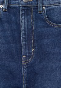 Gros plan de la taille d’un jean en denim bleu avec bouton, passants de ceinture, poche avant et coutures orange visibles.