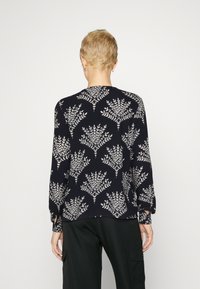 Blusa navy con motivo floreale bianco, maniche lunghe e scollatura rotonda. Tessuto leggero e texture con polsini elastici.