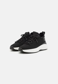 Scarpe sportive nere con una tomaia in rete testurizzata, lacci rotondi e una suola bianca imbottita. Presentano un logo nero a contrasto sul lato.