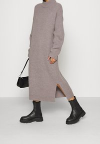 Ljust grå ribbad stickad klänning med hög krage, långa ärmar, sidoficka och en avslappnad passform, kombinerad med svarta platåankelboots och en svart handväska.