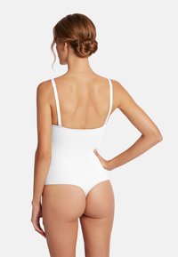 Vit bodysuit med tunna band, rak rygg och högskurna benöppningar, som har ett mjukt tyg och en sömlös design.