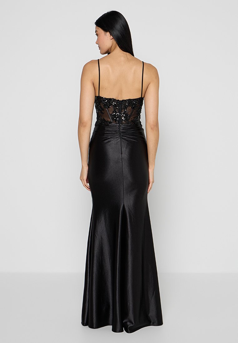 Abito da sera nero con spalline sottili, corpino aderente caratterizzato da una schiena trasparente e impreziosita, e gonna fluttuante con una leggera coda.