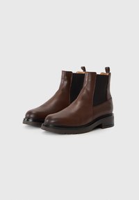 Bottines Chelsea en cuir marron avec une finition texturée, des panneaux latéraux élastiques et un petit talon empilé, dotées de languettes sur le dessus.