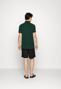 Tmavě zelené polo tričko s krátkými rukávy a límečkem, nošené s černými šortkami a černými nazouváky. Jednoduchý a ležérní vzhled.