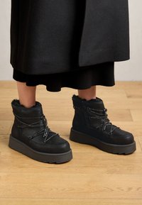 Bottines noires avec une finition texturée, un design à lacets et une semelle épaisse et robuste. Doublées de fourrure douce et dotées d'une fermeture éclair.