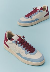 Paire de baskets basses avec des empiècements crème, bleu clair et bordeaux, et des lacets bordeaux sur fond bleu clair.