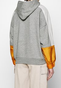 Hoodie gris avec une finition texturée, doté de manches en satin orange et d'un panneau gris clair sur les épaules. Comprend une capuche et un ourlet côtelé.