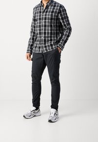 Zwart-wit geruite blouse met knopen, zwarte cargobroek en zilveren sportschoenen met zwarte accenten. De broek heeft zijzakken.