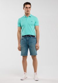 Tirkīza krāsas polo krekls ar apkakli, kombinēts ar gaiši ziliem džinsu šortiem. Akcentēts ar tumši zilu jostu un baltām sporta kurpēm. Ikdienišķa vasaras apģērba izvēle.