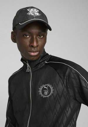 Chaqueta negra con cremallera y patrón de chevron texturizado, con logotipo plateado y gorra a juego con detalle del logo. Ajuste elegante, diseño deportivo.