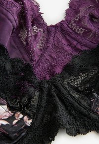 Paarse en zwarte kant lingerie met bloemmotieven, verfijnde details en contrasterende texturen. Het ontwerp benadrukt zachtheid en elegantie.