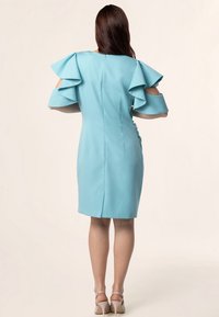 Une robe moulante en tissu bleu clair dotée de manches volantes, d'une fermeture éclair au dos et d'un ourlet mi-long avec une fente à l'arrière.