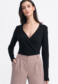 Czarny bodysuit z długim rękawem, głębokim dekoltem w kształcie litery V i owiniętym fasonem, zestawiony z różowymi spodniami o wysokim stanie z przodu z zakładkami i zapięciem na guzik.