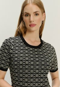 Czarny i kremowy top z wzorem, dzianinowy, z krótkimi rękawami, prążkowanym dekoltem oraz teksturowanym materiałem z geometrycznymi wzorami.