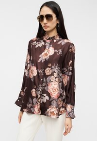 Λουλουδένιο μπλουζάκι από σκούρο καφέ σατέν· διαθέτει ρόζ και γκρι τριαντάφυλλα, ασημένια κουμπιά και γιακά με μακριά μανίκια.