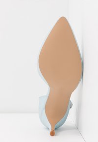 Chaussure à talon haut bleu clair à bout pointu avec une tige texturée et une semelle extérieure en caoutchouc beige lisse, avec un petit accent orange sur le talon.