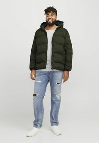 Chaqueta acolchada verde oscuro con capucha, suéter gris debajo, jeans desgastados de color azul claro y zapatillas blancas. Atuendo casual.