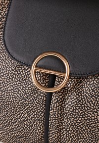 Black faux leather handbag with a patterned beige fabric. Features a gold circular hardware accent and stitched edges.