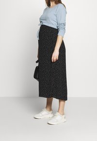 Těhotenské šaty se světle modrým vrškem a černou sukní s bílými puntíky; doplněné bílými teniskami a malou černou kabelkou.