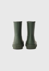 Bottes de cheville en caoutchouc vert avec une texture lisse, des lignes verticales en relief et une semelle plate et robuste. Logo embossé à l'arrière.