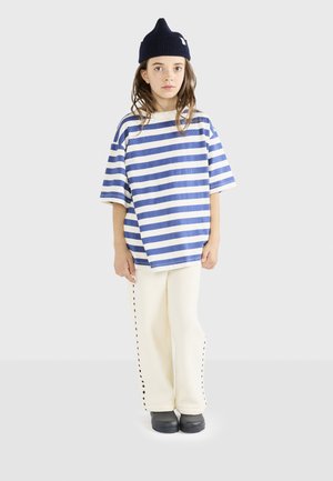 Randig blå och vit oversized t-shirt, krämfärgade byxor med svart sidsöm, och en marinblå mössa. Svarta skor fulländar outfiten.