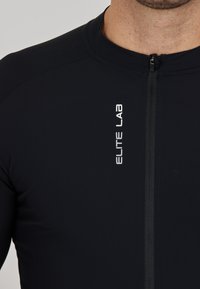Zwart sportief fitted top van glad materiaal, met een ritsluiting en het logo "ELITE LAB" in het wit aan de voorkant.