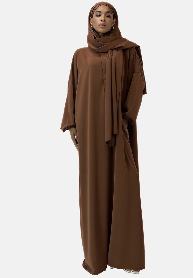 Brun, flödande abaya gjord av mjukt tyg, har långa ärmar, hög halsringning och en matchande hijab, vilket skapar en enhetlig look.